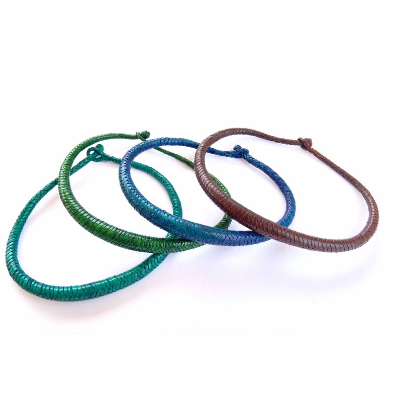 May include: Three leather cord necklaces in shades of green, blue, and brown. The necklaces are braided and have a simple knot closure.