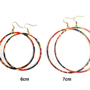May include: Two pairs of hoop earrings. The earrings have a gold-colored hook and a circular hoop design. The hoops are decorated with a pattern of red, navy, and gold. One pair is 6 cm in diameter, and the other is 7 cm.