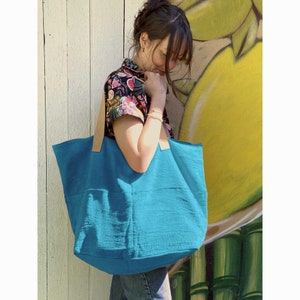 Puede incluir: Un bolso tote turquesa con asas de cuero. El bolso est&aacute; hecho de una tela suave y texturizada y tiene un interior espacioso.