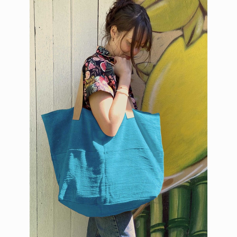 Puede incluir: Un bolso tote turquesa con asas de cuero. El bolso est&aacute; hecho de una tela suave y texturizada y tiene un interior espacioso.