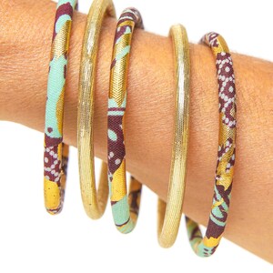May include: Five gold bangles with a patterned fabric covering. The fabric is a mix of brown, green, and gold.