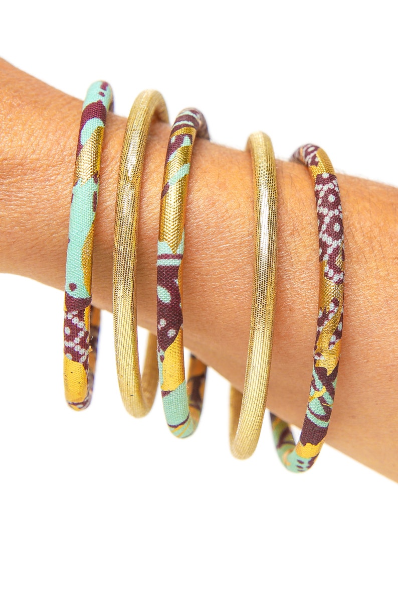 May include: Five gold bangles with a patterned fabric covering. The fabric is a mix of brown, green, and gold.