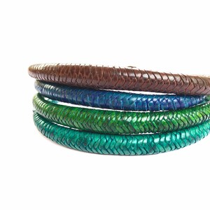 May include: Four leather cords in different shades of green and brown, braided together in a circular shape.