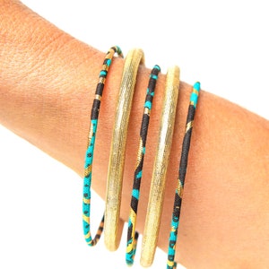May include: Five gold and black bangles with turquoise accents. The bangles are stacked on a person's wrist.