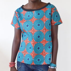 May include: A woman wearing a short-sleeved shirt with a blue and red geometric pattern and denim shorts. She is wearing several bracelets on her wrists.