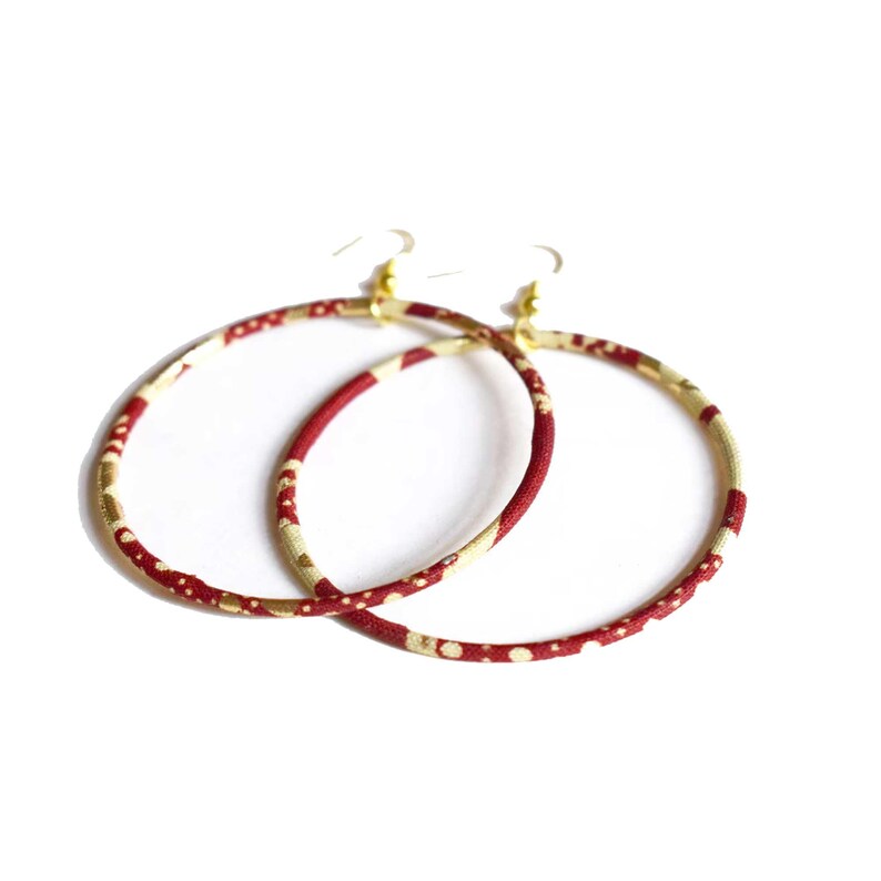 May include: A pair of large hoop earrings. The hoops are covered in a fabric with a pattern of red and gold dots and lines. The earring hooks are gold-colored.