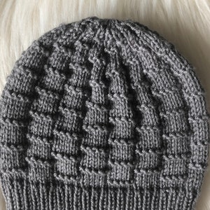 May include: A gray knitted beanie with a textured pattern. The beanie is made of a soft, warm yarn and has a classic, timeless design.