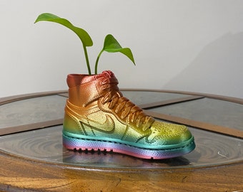 May include: A rainbow-colored high-top sneaker planter with a small green plant growing out of it. The sneaker is sitting on a wooden table.