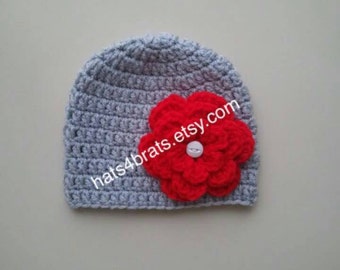 Op de afbeelding: Grijze gebreide muts met een rode gebreide bloem en een witte knoop.