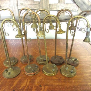 May include: A collection of eight vintage brass-toned metal street lamp miniatures, each featuring a curved arm, a small downward-facing shade, and a circular base with two small protruding metal bolts, arranged in two rows on a wooden surface.