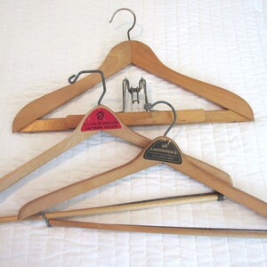 May include: Three wooden hangers with metal hooks. The top hanger has a label that says "Ernest & Edwards, Fashion Village". The middle hanger has a label that says "Capriccio Milano". The bottom hanger has a label that says "Lauterstein's, Fine Clothing Trade".