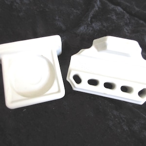 Peut inclure: Deux accessoires de salle de bain en céramique blanche. L'un est un porte-savon carré avec un centre évidé. L'autre est un porte-brosse à dents rectangulaire doté de quatre ouvertures ovales distinctes sur le bord avant pour ranger des objets.