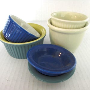 May include: Four ceramic bowls in various sizes and colours. The bowls are stacked on top of each other. The top bowl is white, the next bowl is green, the next bowl is yellow, and the bottom bowl is blue.
