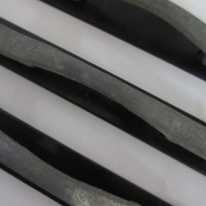 May include: Three cabinet pulls featuring a matte black rectangular base plate and a textured gray arched handle. Each handle is securely mounted to the center of the black plate, creating a contrast between the dark finish and the lighter gray surface.