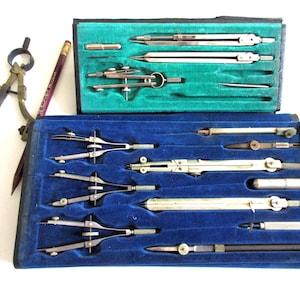 May include: A vintage drafting set featuring various metal compasses, dividers, and drawing tools housed in two separate cases with blue and green velvet linings. A single brass and steel compass and a wooden pencil are positioned to the left.