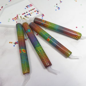 Könnte beinhalten: Vier farbige Diamant-Malwerkzeuge mit regenbogenfarbenen Streifenmustern und durchsichtigen Kunststoffspitzen.