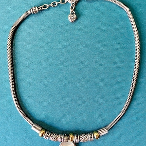 May include: A silver-toned snake chain necklace featuring a central pendant with a round, iridescent white shell-like stone. The necklace includes alternating gold and silver-toned textured beads and a lobster claw clasp with an extender chain.