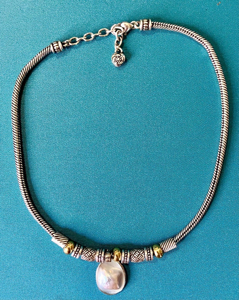 May include: A silver-toned snake chain necklace featuring a central pendant with a round, iridescent white shell-like stone. The necklace includes alternating gold and silver-toned textured beads and a lobster claw clasp with an extender chain.