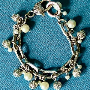 May include: A silver-toned chain link bracelet featuring a heart-shaped clasp and alternating charms. The charms consist of round white faux pearls and small, textured silver-toned spheres. The bracelet links have an engraved pattern.