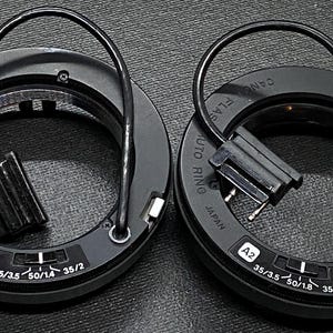 May include: Two black flash ring adapters with cords and connectors. The adapters have markings for "AUTO RINO" and "FLASH", as well as "JAPAN" and "35/3.5 50/1.4 35/2".