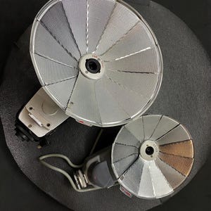 May include: Two silver and gold flash diffusers for a camera flash. The larger diffuser has a silver finish and the smaller diffuser has a silver and gold finish.