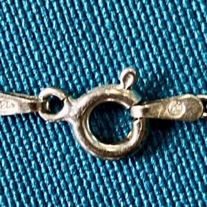 May include: A silver-colored metal spring ring clasp attached to a delicate chain. The clasp mechanism features a small lever and a circular ring. One side of the clasp connector is stamped with the number 925, indicating sterling silver content.
