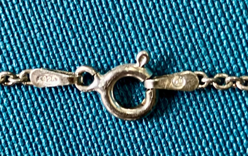 May include: A silver-colored metal spring ring clasp attached to a delicate chain. The clasp mechanism features a small lever and a circular ring. One side of the clasp connector is stamped with the number 925, indicating sterling silver content.