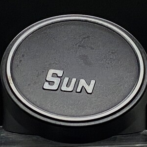 Puede incluir: Un altavoz redondo negro con un borde plateado y la palabra "SUN" impresa en letras plateadas.