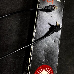 May include: Black and white box with red starburst logo for a Vivitar PC-1 30-inch shutter cord. The cord is black and has a right-angle connector on one end and a straight connector on the other end.