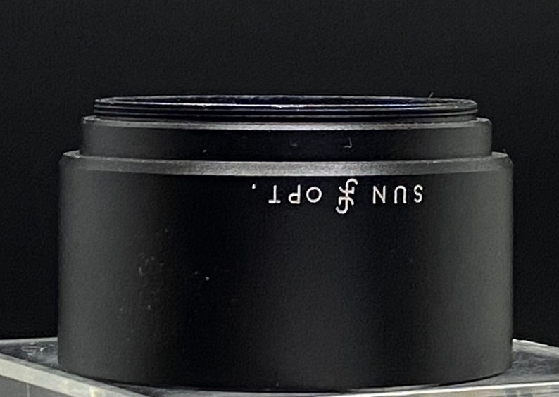Puede incluir: Tapa de lente negra con el texto "SUN OPT." impreso en blanco.