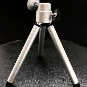 May include: A silver tripod with adjustable legs and a rotating head. The tripod is small and compact, making it ideal for use with a smartphone or small camera.