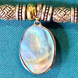 May include: A necklace featuring an oval pendant with an iridescent, pearlescent surface set in a silver-toned frame. The chain consists of alternating silver-toned beads with woven textures, smooth cylindrical spacers, and a single gold-toned bead.