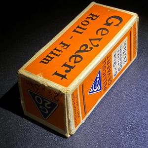 May include: Vintage Gevaert roll film box. The orange box features the brand name and product details in black and white text. The box is labeled "Roll-Film" and "Orthochromatique Anti-Halo". The box measures 2 1/4 x 3 1/4 inches.