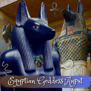 May include: A blue statue of the Egyptian goddess Anput, depicted as a jackal-headed woman, with a gold ankh symbol above her head. The statue is wearing a beaded necklace and has a detailed, textured surface.