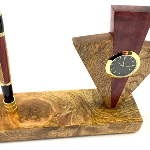 May include: A wooden desk organizer with a clock and a pen holder. The clock has a black face and gold hands. The pen holder is made of wood with a red and black pattern. The organizer is made of wood with a brown and gold finish.