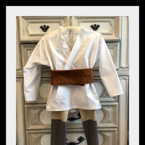 Op de afbeelding: Een wit kostuum met een bruine riem en colorblock broek. De top is een wikkelshirt. De broek heeft tan en bruine panelen. De Etsy shop naam en website zijn zichtbaar onderaan de afbeelding.