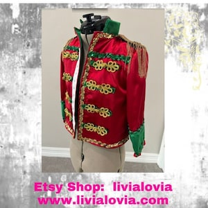 May include: A red jacket with gold and green accents, displayed on a mannequin. The jacket features gold trim, decorative gold clasps, and green cuffs and collar. The Etsy shop name and website are visible at the bottom.