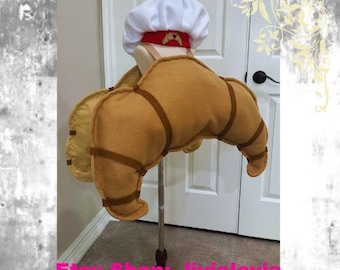 May include: A brown felt croissant costume with a white chef hat and a red and gold badge. The costume is on a stand and is ready to be worn.