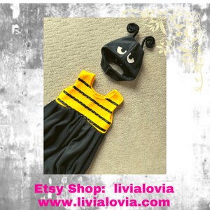 May include: A black and yellow baby bee costume set. The set includes a black jumpsuit with yellow stripes and a matching black hat with antennae and white eyes. The Etsy shop name and website are visible in the image.