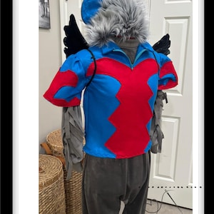 May include: A blue and red costume with gray wings and a gray furry head. The costume has a zipper in the front and a black cord around the neck. The costume is worn by a person, but the person's face is not visible.