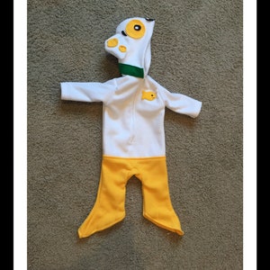 May include: A white and yellow baby outfit resembling a duck. The hooded jumpsuit features a duck head with yellow eyes and beak, a green collar, and a small yellow fish applique. The bottom half is yellow.
