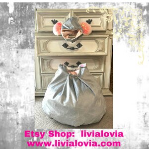 May include: A silver-gray baby play mat and matching hooded hat with pink lining and ear accents. The play mat is round and gathered at the top. The hat has pink ear accents. The Etsy shop name and website are displayed at the bottom.