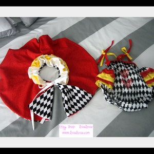 May include: A red and white checkered baby onesie with yellow trim and a red heart. The onesie is paired with a red cape with a white and black checkered trim.