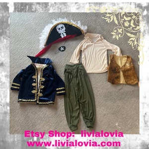 Puede incluir: Un conjunto de disfraz de pirata para niños, que incluye una chaqueta de terciopelo azul con ribetes dorados, un sombrero de pirata blanco y rojo, una camisa beige, pantalones verdes y un chaleco marrón.