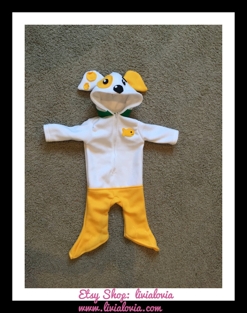 May include: A white and yellow dog-themed baby onesie with a hood featuring a dog face design. The onesie has a zipper closure, green trim, and a small fish applique. The legs are yellow.