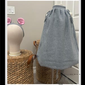 Puede incluir: Un saco de dormir gris con capucha y cierre de cordón. El saco de dormir está en un maniquí y se muestra contra una pared blanca.