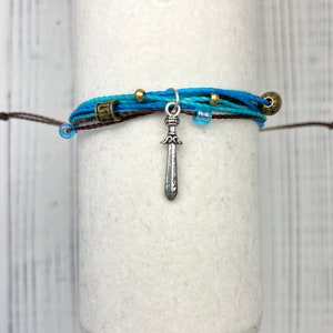 May include: A blue and brown friendship bracelet with a silver sword charm and gold and blue beads.