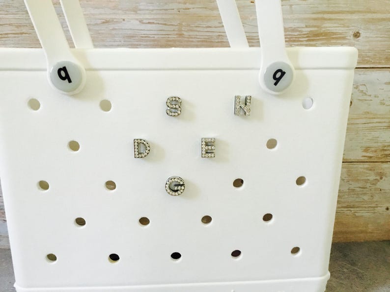 Peut inclure: Sac fourre-tout blanc avec une grille de trous et des strass qui &eacute;pellent le mot "SEND" au centre. Le sac a deux poign&eacute;es avec un bouton blanc sur chaque poign&eacute;e qui dit "Q".