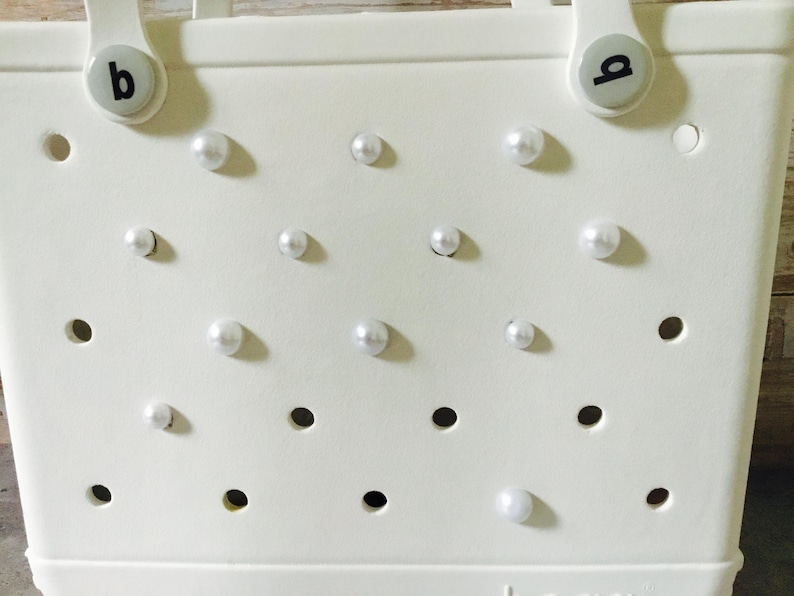 May include: White tote bag with a  'b' on each handle and a pattern of white pearl-like embellishments.