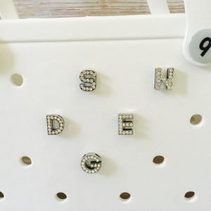 Peut inclure: Cinq lettres blanches avec des strass qui &eacute;pellent le mot "SDEG" sur un fond blanc.